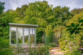 Salthouse Studio Garden Office Contemporary grey garden office with full-height glazing, nestled among mature trees and colourful garden planting.